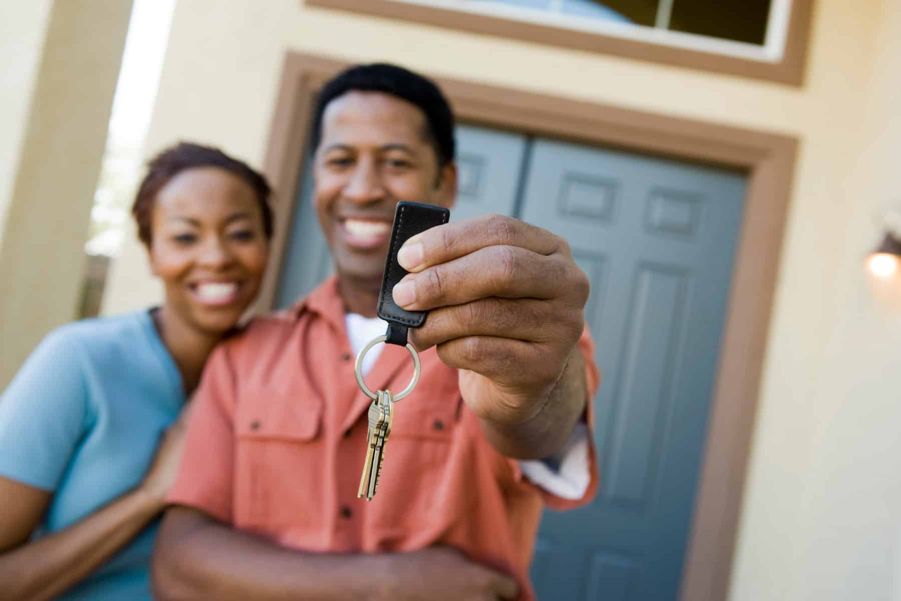 First-time home buyers standing in front of a new home holding the keys